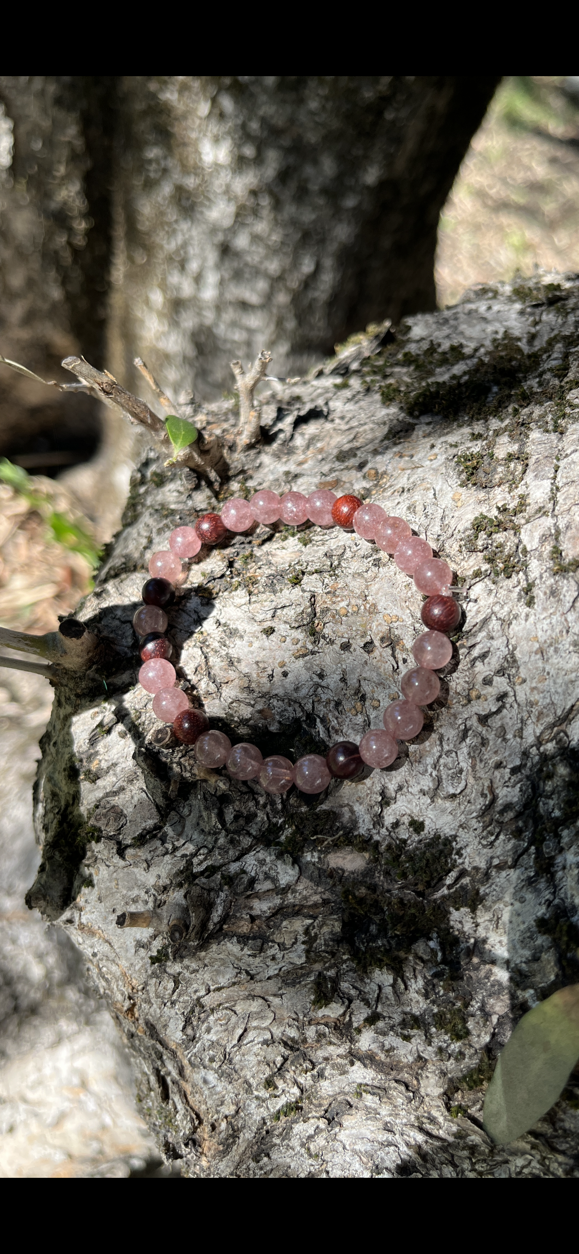 bracelet en pierres naturelles de quartz fraise et bois de santal posé sur un rocher