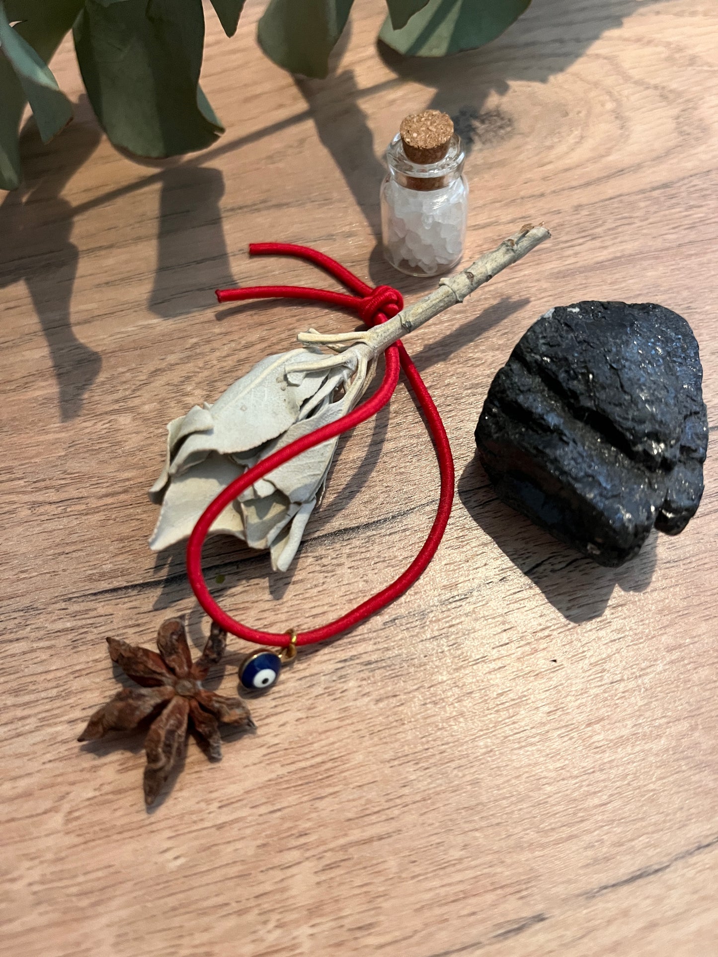 pierre de tourmaline noire fiole sel Himalaya bâton de sauge bracelet rouge oeil de protection étoile de cannelle posés sur une table