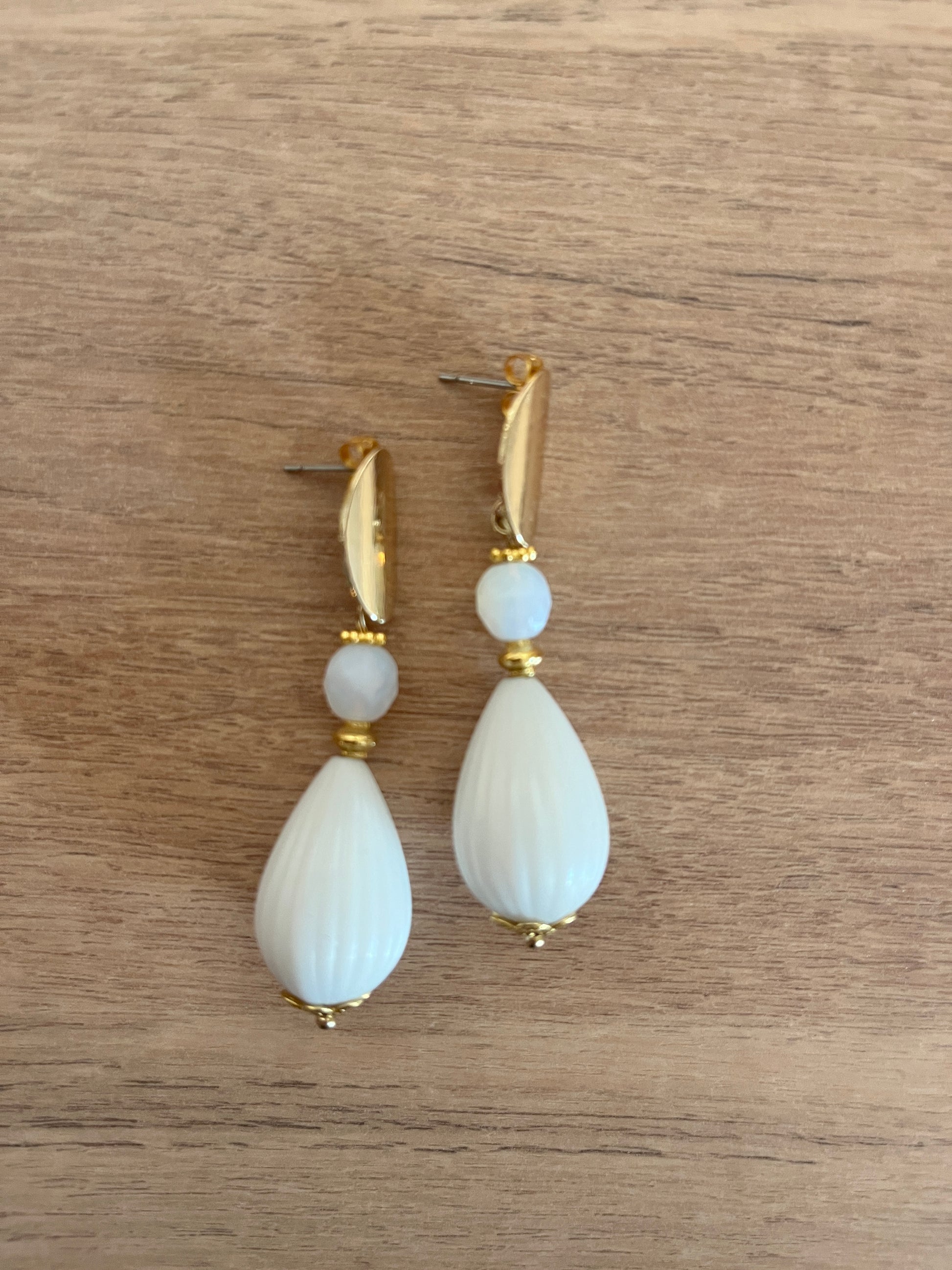 boucles d oreilles pendantes blanches et acier inoxydable doré posées sur une table en bois 