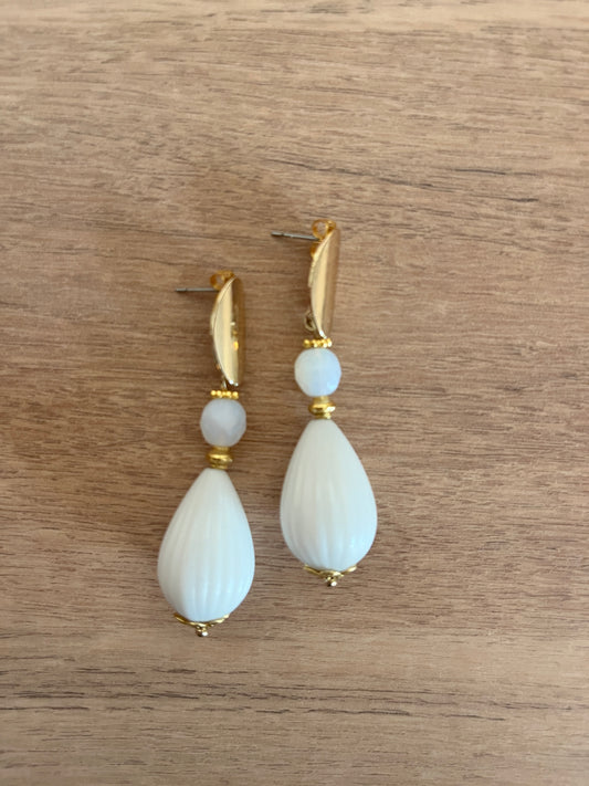 boucles d oreilles pendantes blanches et acier inoxydable doré posées sur une table en bois 